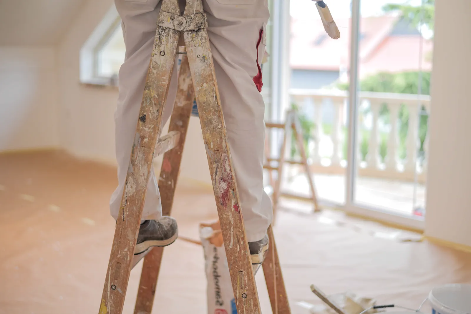 Pintor subido a una escalera de madera en una habitación con balcón